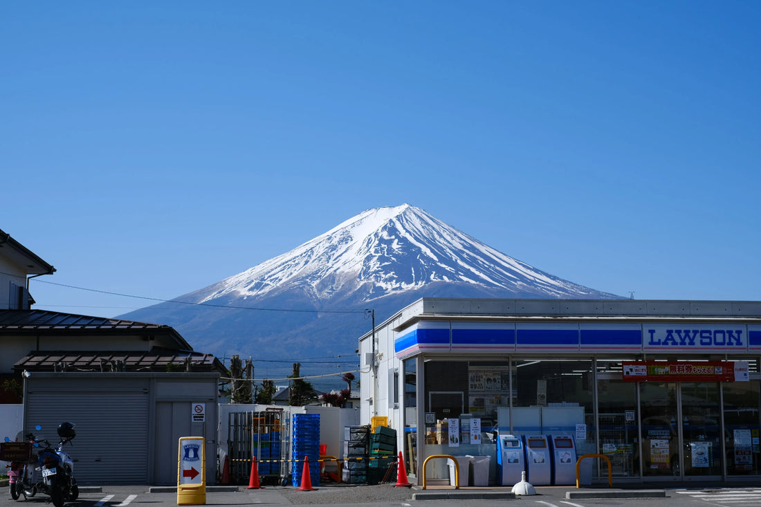 A beautiful view of Mount Fuji seen from behind a convenience store under a clear blue sky.