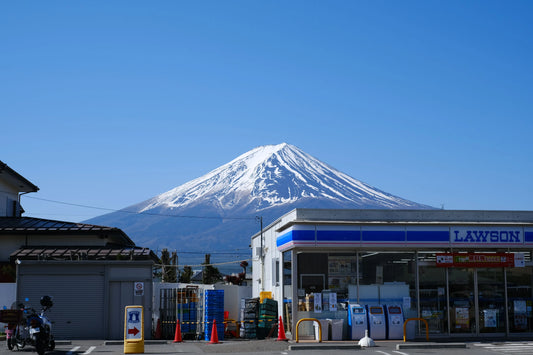 A beautiful view of Mount Fuji seen from behind a convenience store under a clear blue sky.